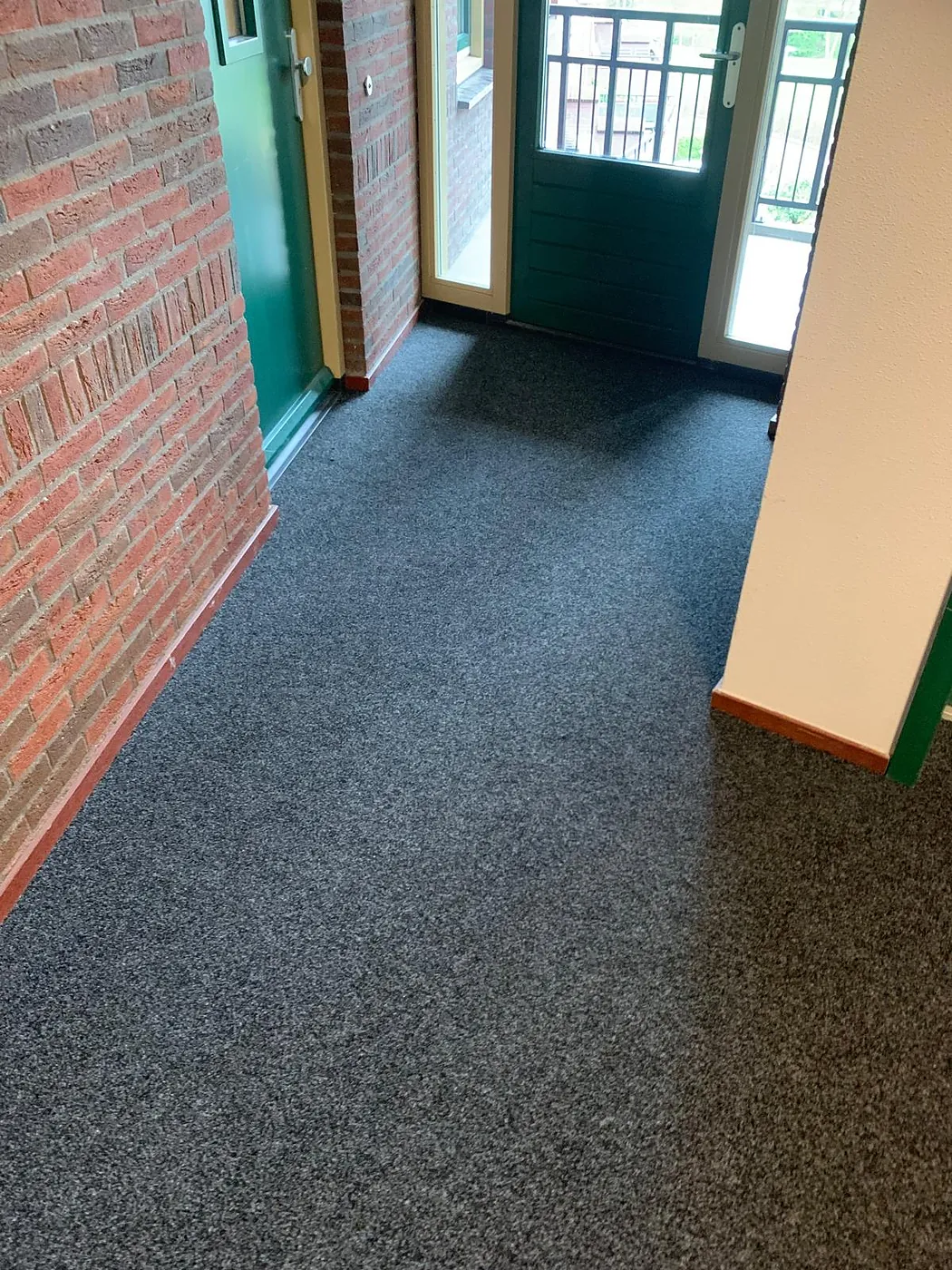 Antracietgrijze tapijtvloer in een hal met karakteristieke bakstenen muur
