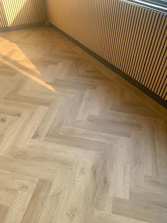 Lichte eiken visgraatvloer met zonlicht langs een houten lattenwand